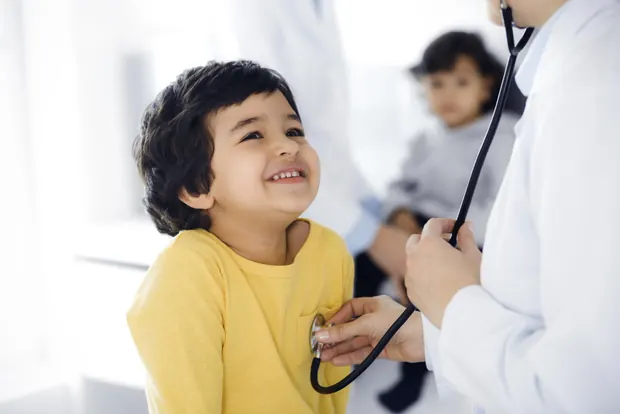 A doctor examining a smiling young child with a stethoscope during a paediatric consultation